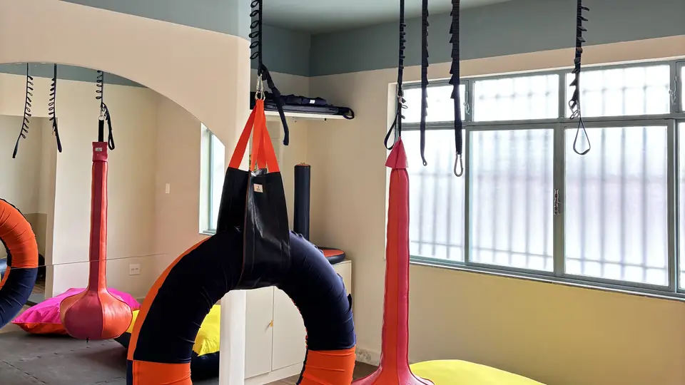 Sala de integração sensorial com equipamentos suspensos, tatame e almofadas coloridas